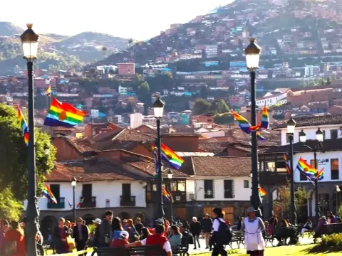 Seven-striped Cusco flags flying in the Plaza de Armas, with urbanized hills in the background