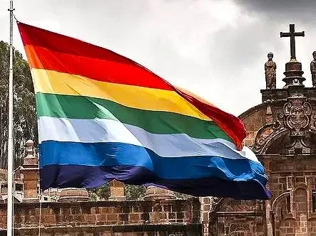 Seven-striped flag of Cusco flying in front of the colonial façade of the Church of the Society of Jesus