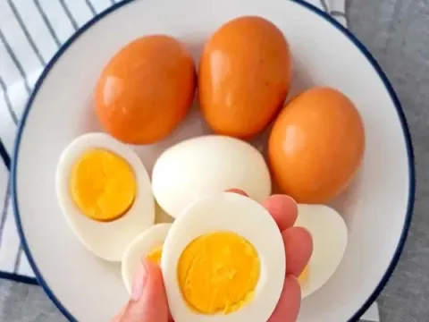 Close-up of sliced and whole hard-boiled eggs with bright orange yolks on a white plate.