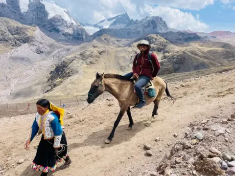 Tourist riding a horse along a mountain trail with a local guide, on the way to Vinicunca, Peru