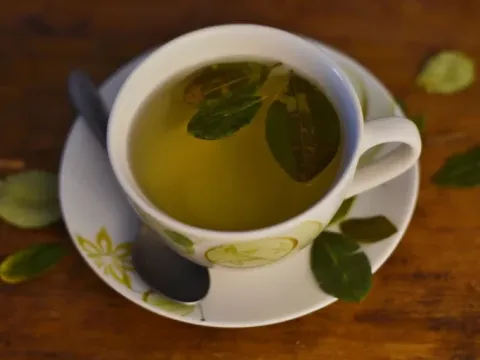 A cup of hot coca leaf tea on a wooden table, used to prevent altitude sickness in the Andes