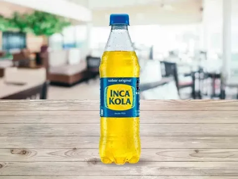 A cold bottle of Inca Kola, the famous Peruvian golden soda, standing on a wooden surface.