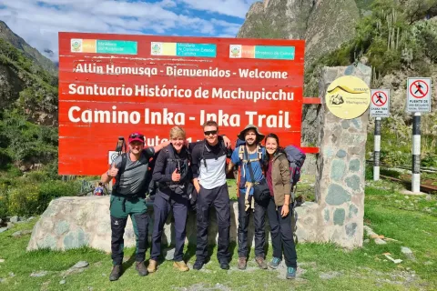 A group of five travelers posing in front of the official "Camino Inka - Inka Trail" sign at the start of the trek in Peru.
