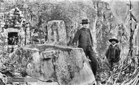 Moment of the "discovery" of Machu Picchu: Explorer Hiram Bingham next to the Inca sundial Historical black and white photograph of Hiram Bingham and a local boy next to the Intihuatana in 1911