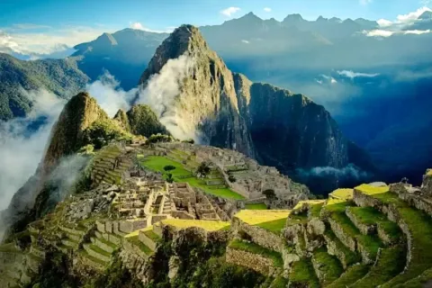 High-angle panoramic view of the Machu Picchu citadel with low clouds and the surrounding Andes peaks.