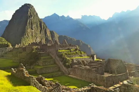 The stone citadel of Machu Picchu illuminated by soft morning light with Huayna Picchu in the background.