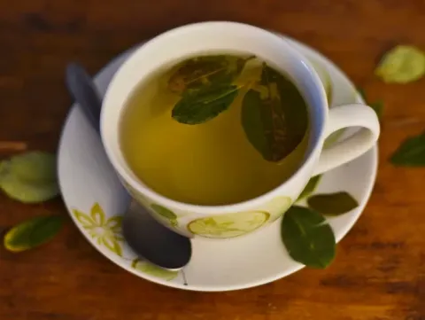A white ceramic cup filled with coca leaf tea, featuring a lime design on the saucer, over a wooden background.