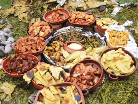 Multiple clay dishes arranged in a circle on the grass, showcasing a variety of meats, tamales, and Andean tubers