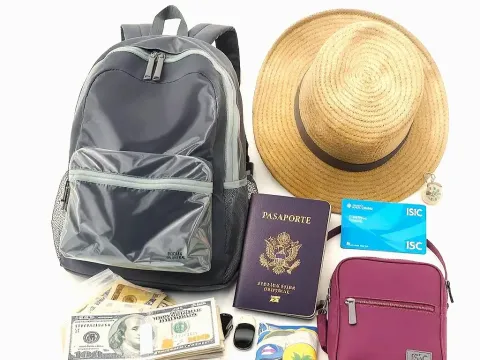 Essential travel items such as passport, money, backpack, and hat, on a white surface