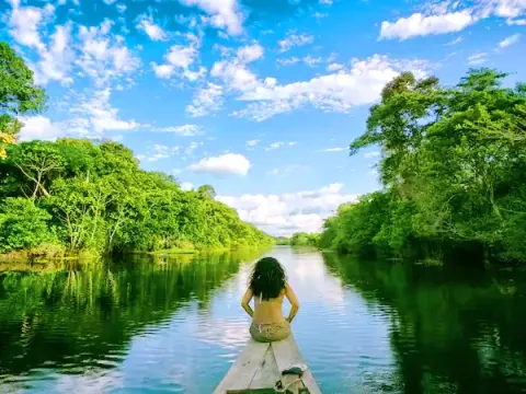 A woman sitting at the front of a boat, looking out at the calm river and lush trees of the Manu rainforest.