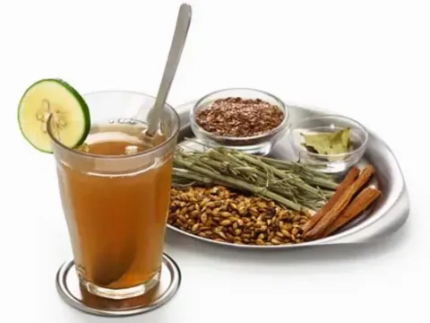 A glass of traditional Peruvian emoliente next to a tray with barley, flaxseed, and medicinal herbs.