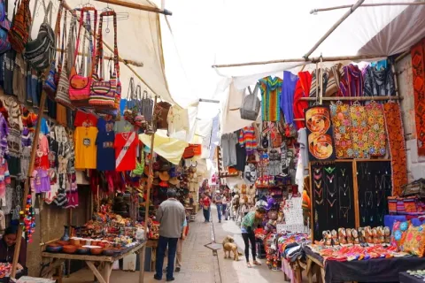 A narrow street in the Pisac market filled with colorful Peruvian ponchos, bags, and handmade souvenirs.