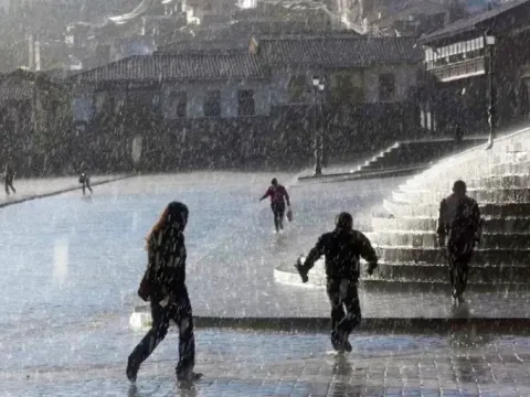 People walking across the wet Plaza de Armas in Cusco during a rainy day in the Andes