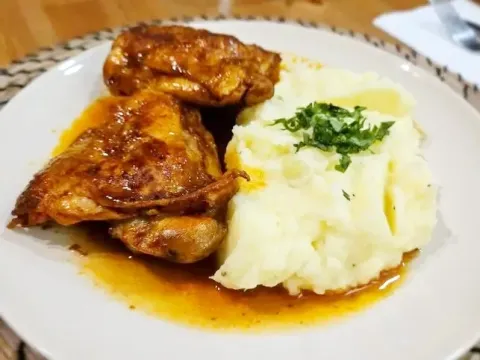 Roasted chicken pieces served with a side of creamy mashed potatoes and a light herb garnish.