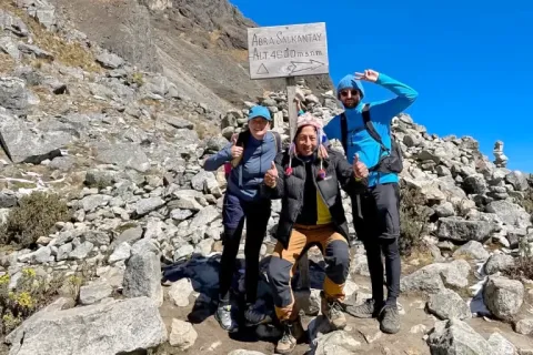 Three happy trekkers celebrating at the Abra Salkantay sign (4,600 meters) during the Salkantay Trek to Machu Picchu.