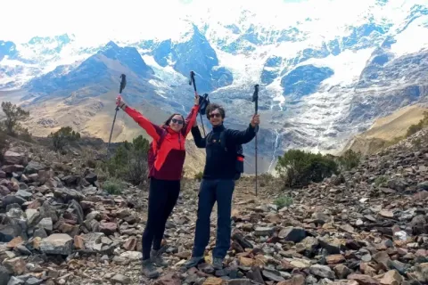 Two hikers celebrating with arms raised in front of the snow-capped Salkantay mountain in Peru.