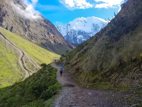 Hikers walking on a mountain trail with the snowy Salkantay peak in the background.