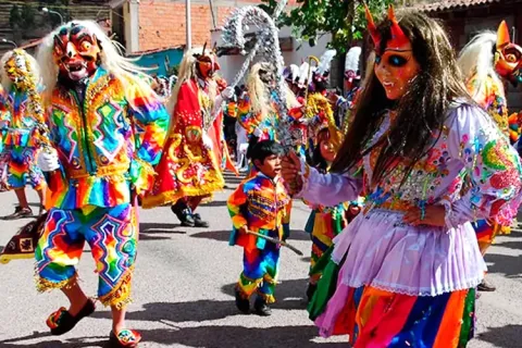 Dancers in colorful Saqra masks and rainbow costumes during a festival in Cusco.