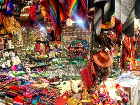 A vibrant market stall filled with Peruvian handicrafts, including chullos, alpaca plushies, and colorful Cusco souvenirs