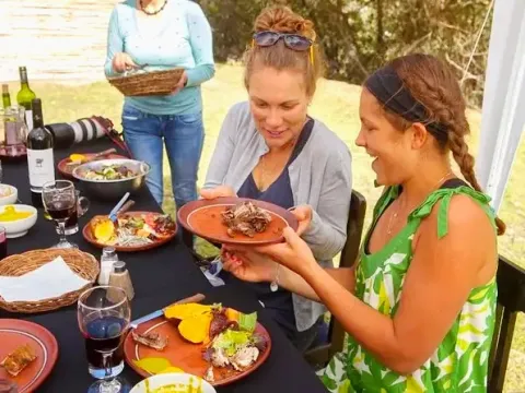 Two female tourists smiling and enjoying a meal of Pachamanca at an outdoor table during a guided tour