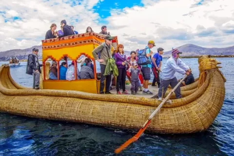 A group of tourists riding a large, traditional yellow totora reed boat on the blue waters of Lake Titicaca.