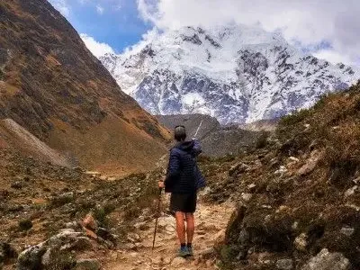 A hiker with trekking poles pointing towards the snowy Salkantay mountain.