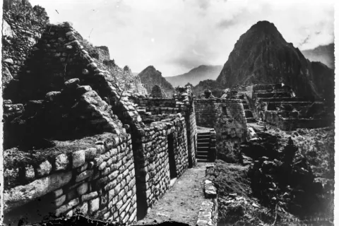 Historic black and white photograph of the ruins of Machu Picchu with Huayna Picchu in the background.