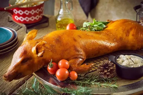 A whole roasted suckling pig garnished with tomatoes on a wooden board.