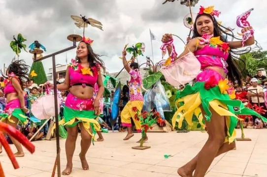 Group of women performing a traditional Amazonian dance in colorful pink and green floral costumes.