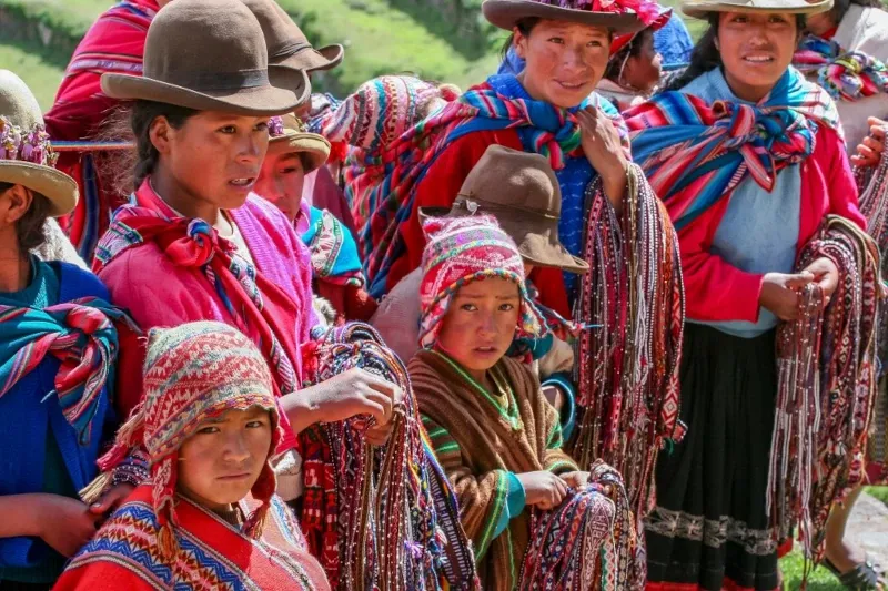Traditional Andean Textiles and Local Culture Local Andean children and women dressed in colorful traditional clothing holding handmade woven textiles in a mountain village near Cusco.