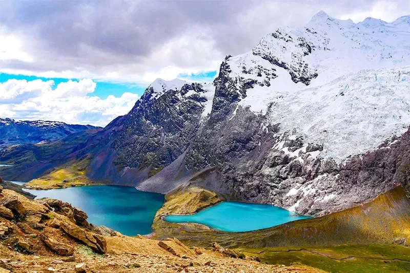 High-angle view of two bright blue glacial lakes nestled between rugged Andean mountains and the snow-covered Ausangate glacier.