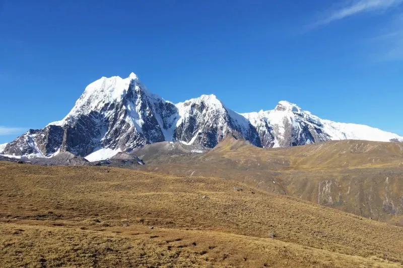 View of the massive Ausangate mountain range with prominent snow-capped peaks and dry highland grass in the foreground.