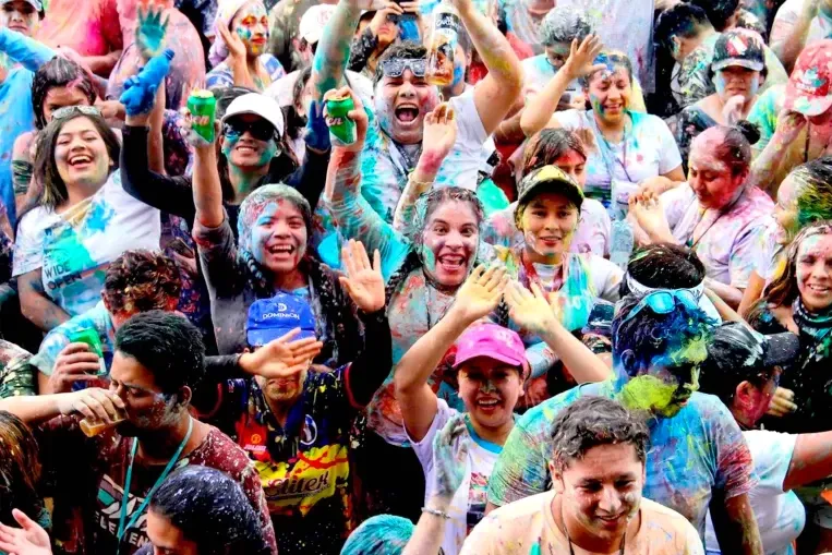 Crowd of people celebrating Peruvian carnival covered in colorful paint and water.