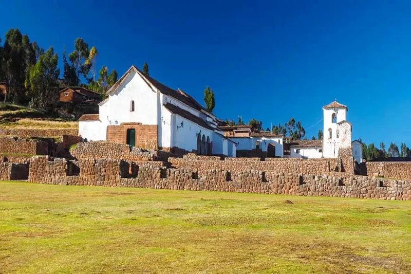 The white colonial church of Chinchero built upon ancient Inca stone foundations under a bright blue sky in the Sacred Valley.