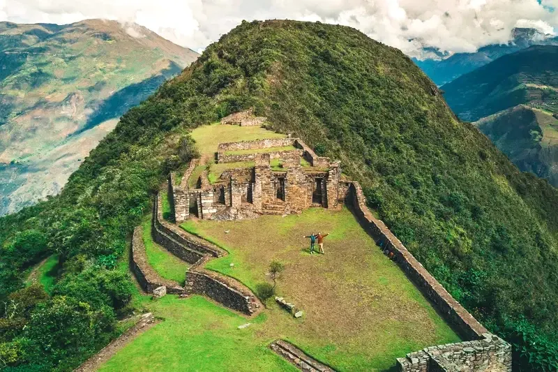 Aerial panoramic view of the Choquequirao archaeological complex, known as the "sister city" of Machu Picchu, surrounded by lush green mountains.