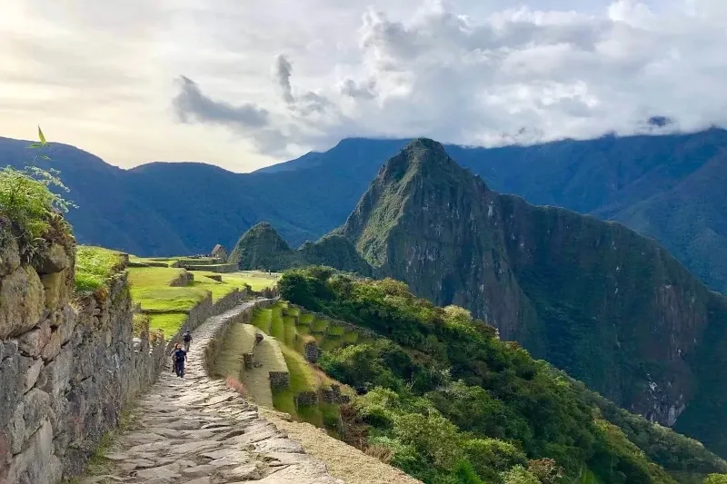 Hikers walking on a historic Inca stone path next to agricultural terraces with the Vilcanota mountain range in the background.