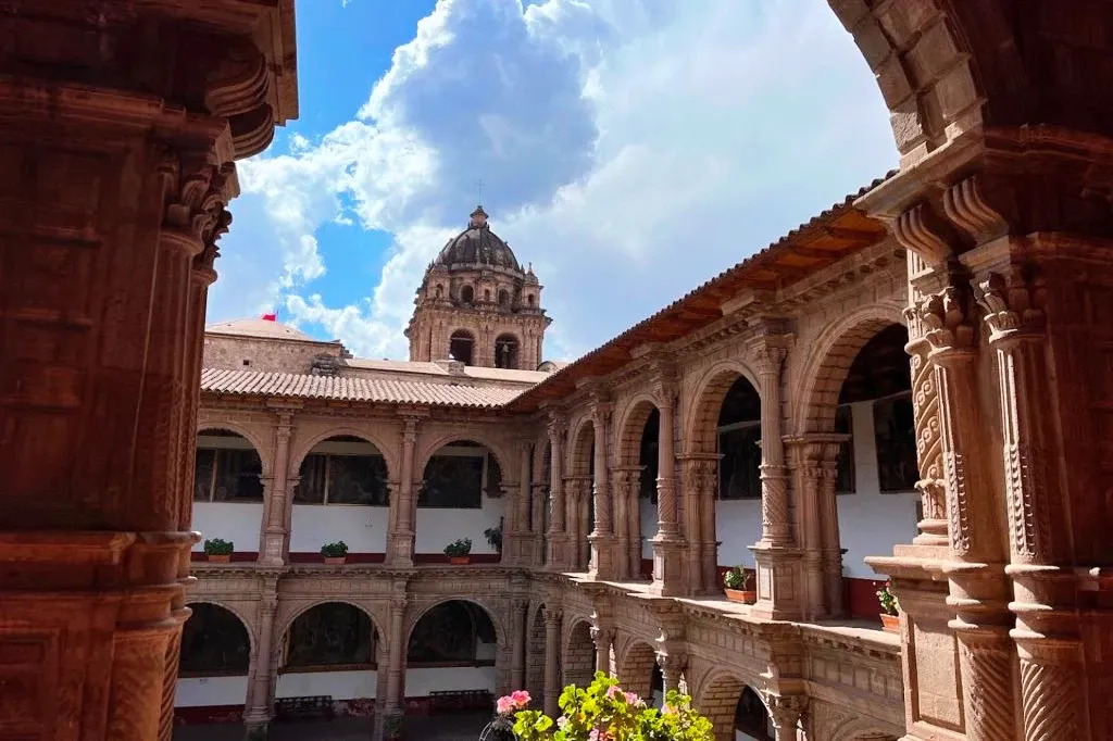 Interior view of a colonial convent courtyard in Cusco with stone arches and a view of a church bell tower.