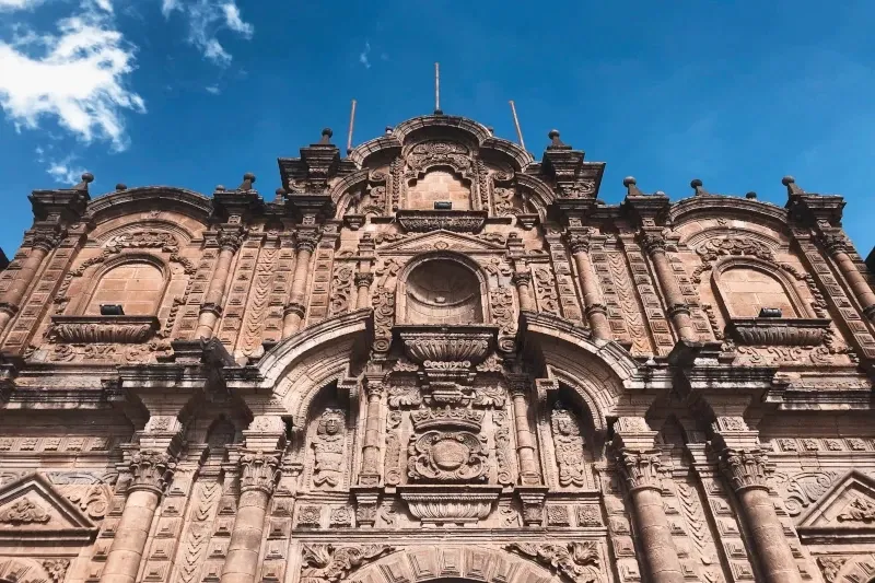Detailed low-angle view of the intricate Andean Baroque stone facade of the Compañía de Jesús Church in Cusco.