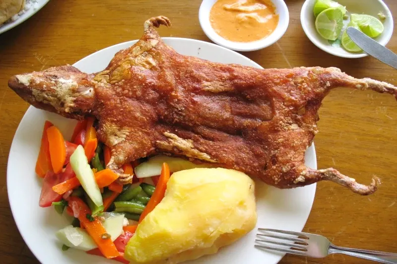 Top view of a perfectly crispy Cuy Chactado served with a side of fresh vegetable salad, a large boiled potato, and spicy dipping sauces.