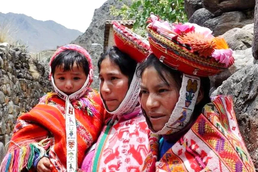 Close-up of an Andean mother and her baby wearing intricate traditional hats and colorful hand-woven ponchos.