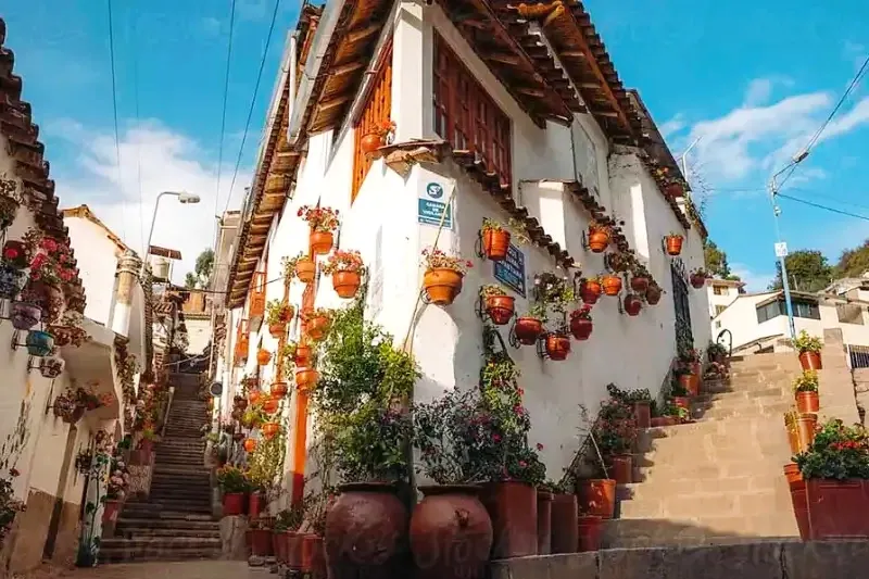 White colonial building on a street corner in Cusco decorated with dozens of hanging clay flower pots under a blue sky.