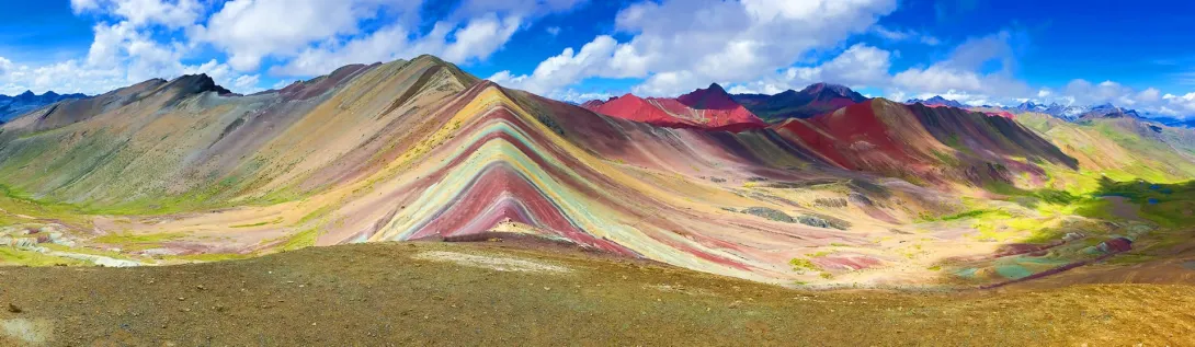 Ultra-wide shot of the entire Vinicunca mountain range showing the red valley and multi-colored geological formations.