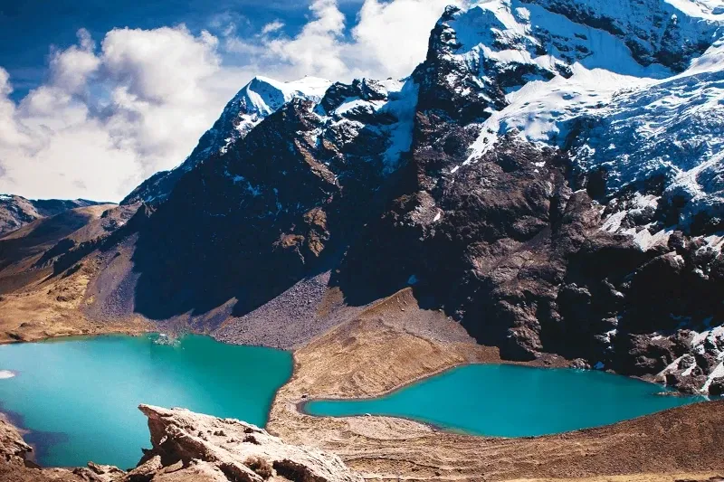 Two bright turquoise lakes separated by a thin strip of land under the massive glaciers of the Ausangate mountain range.