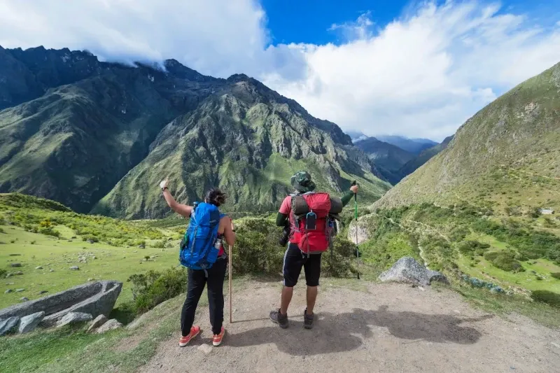 A close-up of hikers near a large carved stone structure on a mountain trail in the Cusco region.