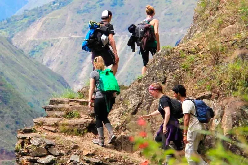 Close-up of adventure travelers climbing steep stone steps on the trek to Machu Picchu surrounded by Andean vegetation.
