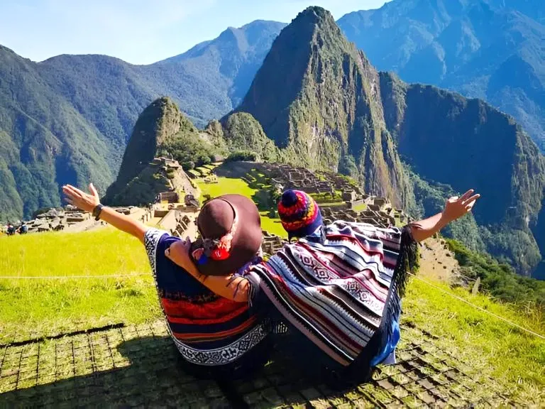 Celebrating at Machu Picchu Two hikers sitting and looking at the Machu Picchu ruins with their arms raised.