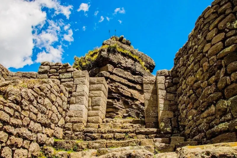 Steep stone stairs leading to the horn-shaped peaks of the Waqrapukara archaeological complex under a bright blue sky.