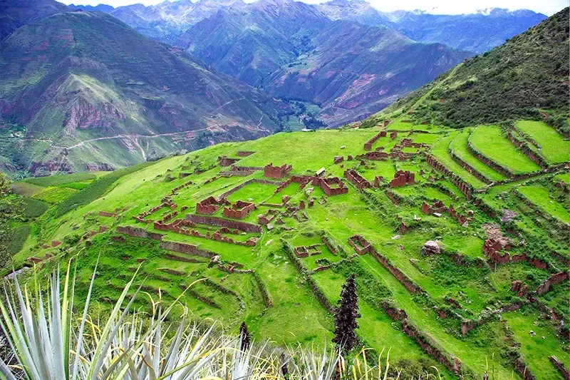 High-angle view of the Huchuy Qosqo stone structures and green terraces overlooking the deep canyons of the Sacred Valley.