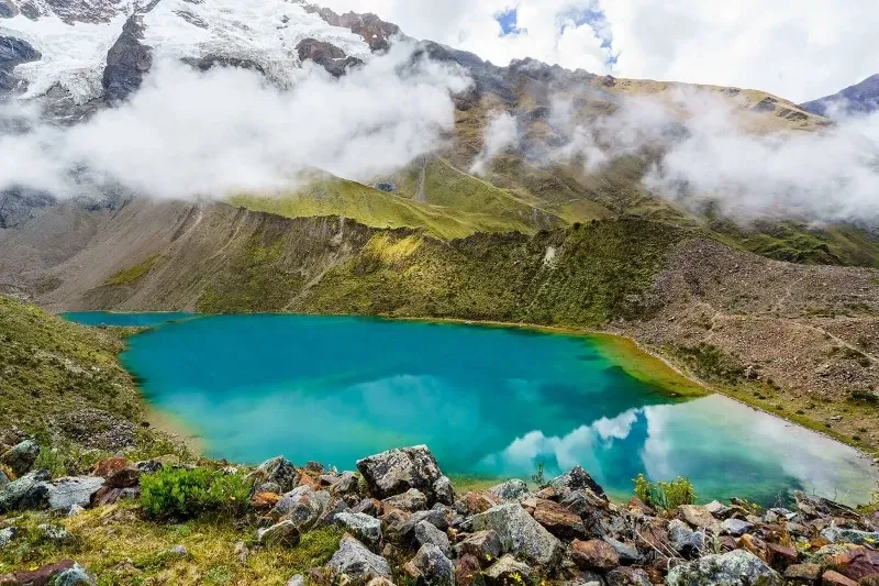 High-angle shot of a turquoise alpine lake surrounded by steep mountains and low-hanging clouds.
