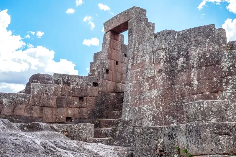 An ancient Inca stone doorway and staircase leading up a hillside under a blue sky.